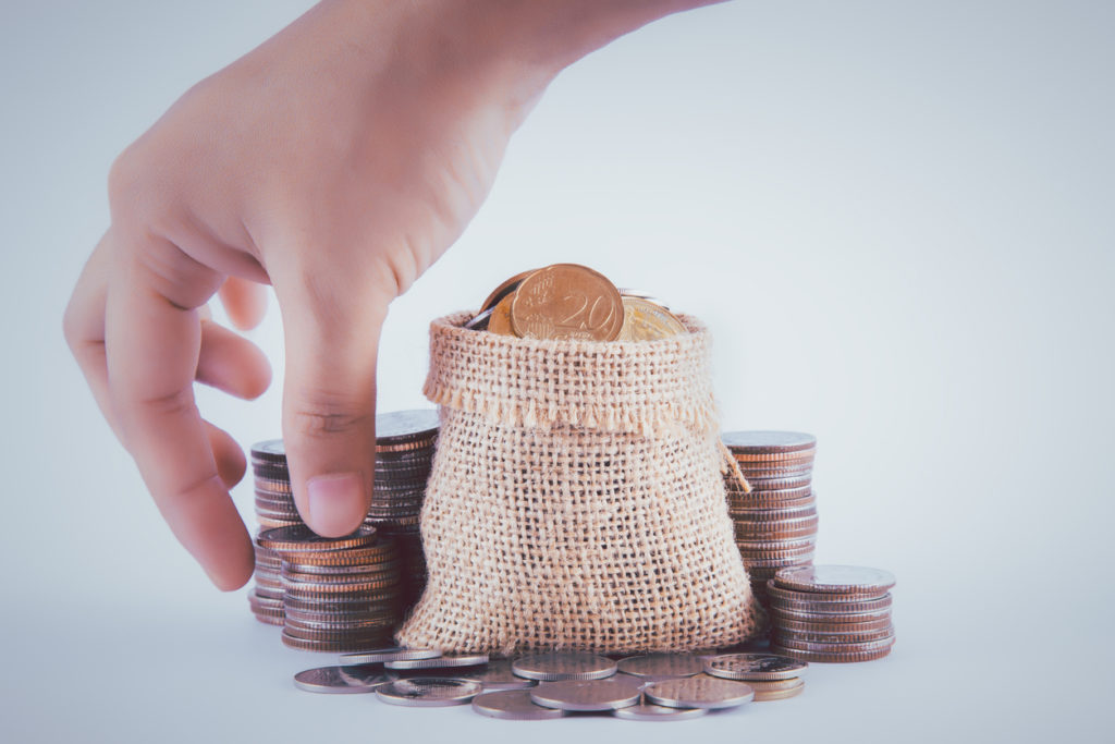 The female hand is picking up coin from the pile of coins and coin in sackcloth.